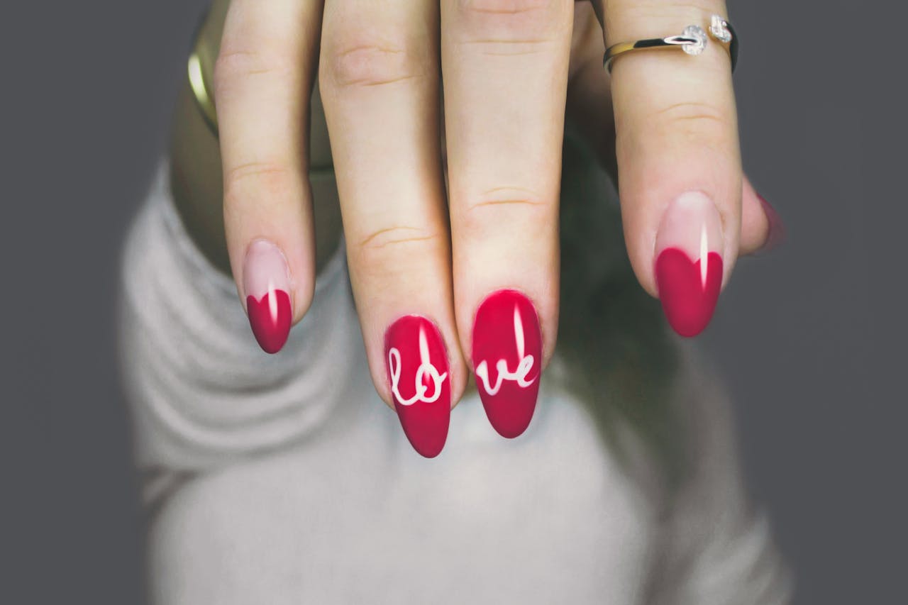 Vibrant red nails with 'love' art on a woman's hand, showcasing elegant style and design.